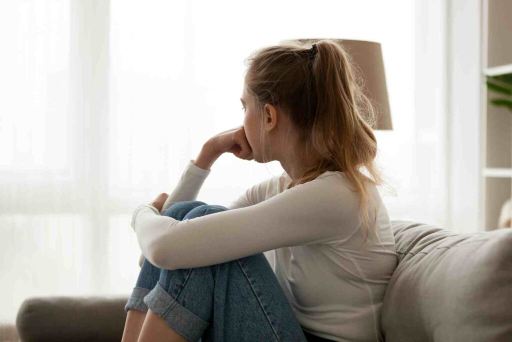 Teen girl sitting on a couch looking out the window while feeling overwhelmed