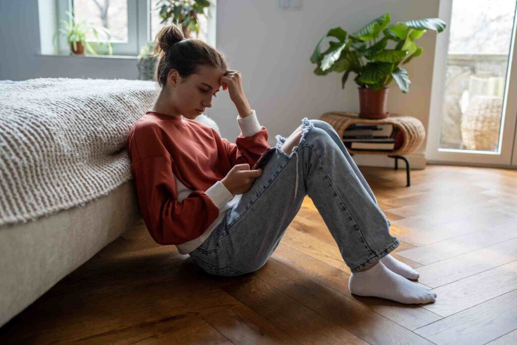 Teen girl sitting on the floor looking at her phone with a stressed expression