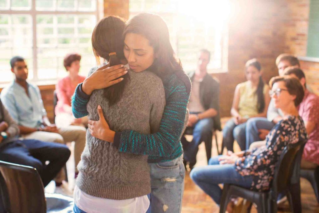 Two women hugging in a group therapy session showing emotional support and recovery