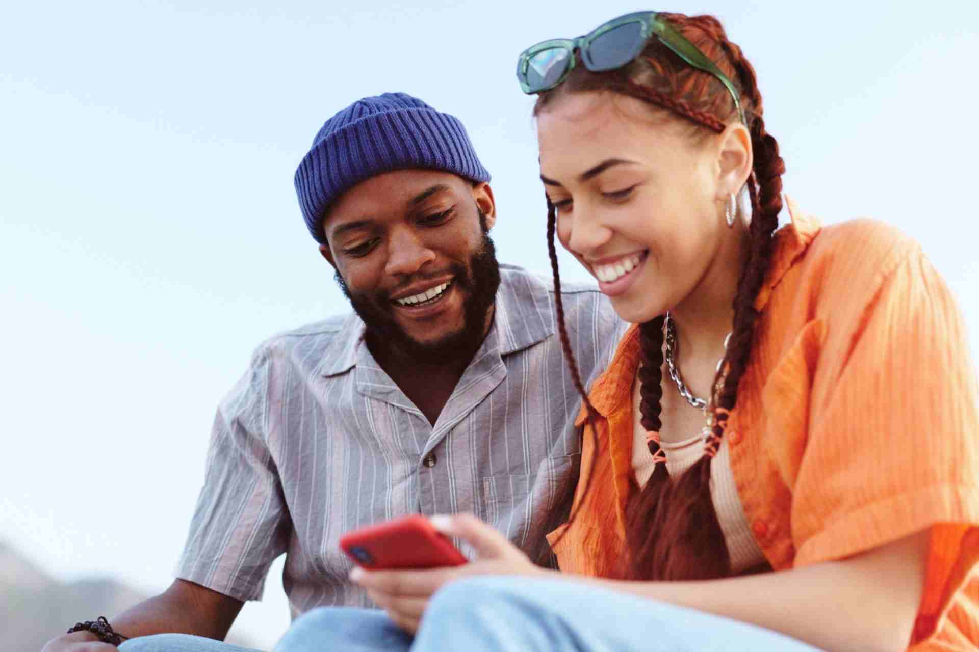 Two young adults smiling while using a smartphone together, representing hope, encouragement, and connection during the recovery journey.