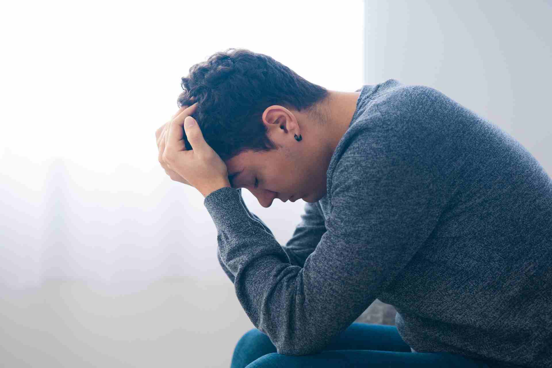 A teenager sits with his head in his hands, showing emotional distress that may be associated with substance use or mental health challenges. Image Description