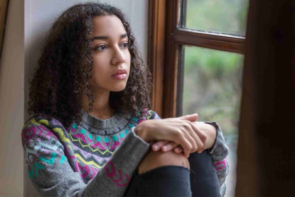 A teenage girl looks thoughtfully out a window, reflecting emotional or behavioral changes that may require support.