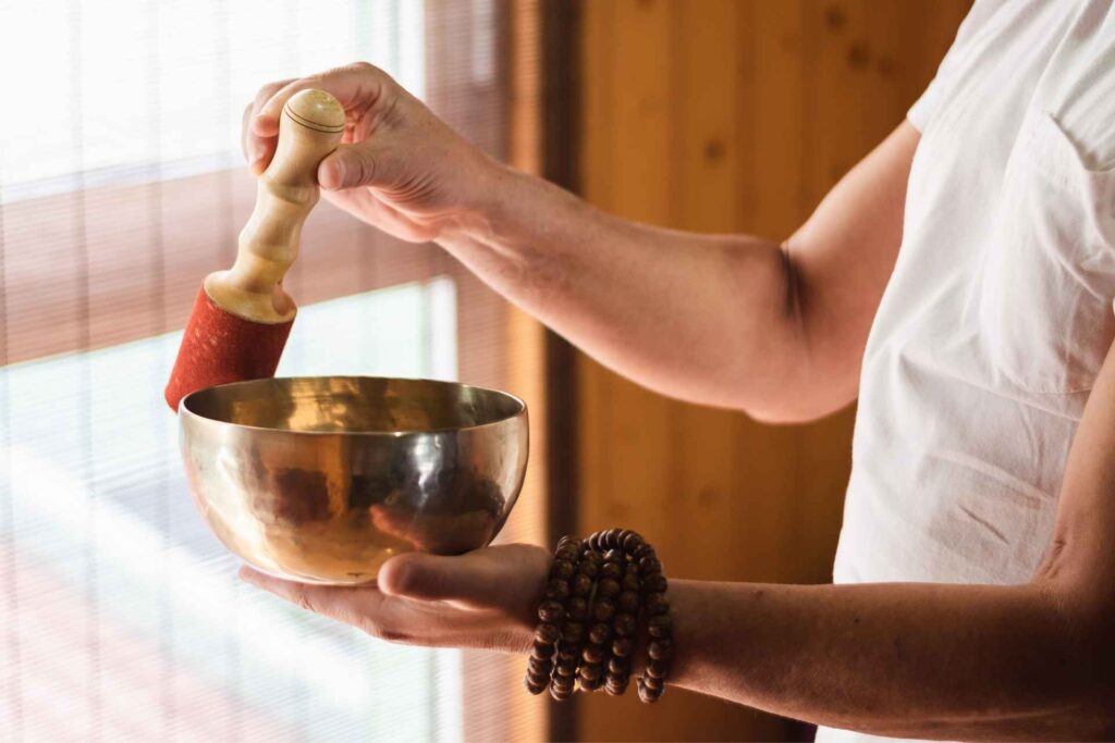 Person holding a Tibetan singing bowl and wooden mallet during a mindfulness practice.